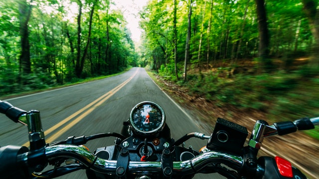 An image of a rider on a motorcycle riding on a street with woods on both sides, showing how Harwood Legal PLLC can has the experience and skill to get compensation for you in your West Virginia motorcycle accident case.